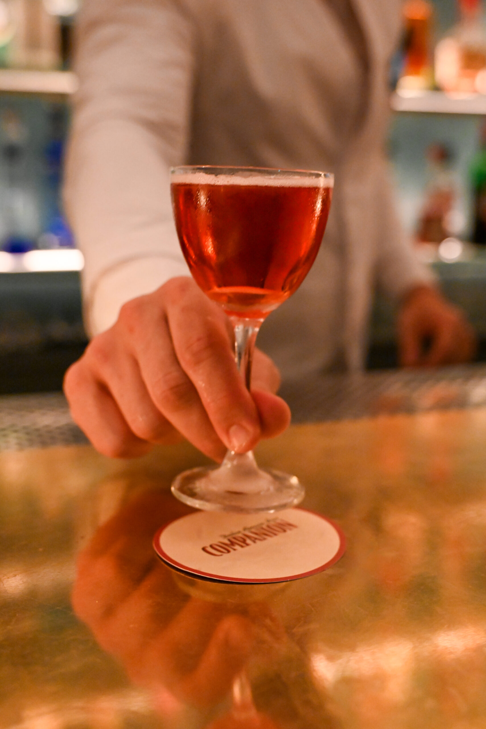 A drink being served by the bartender on a coaster with the logo Companion Dolce Amaro Bar on it.