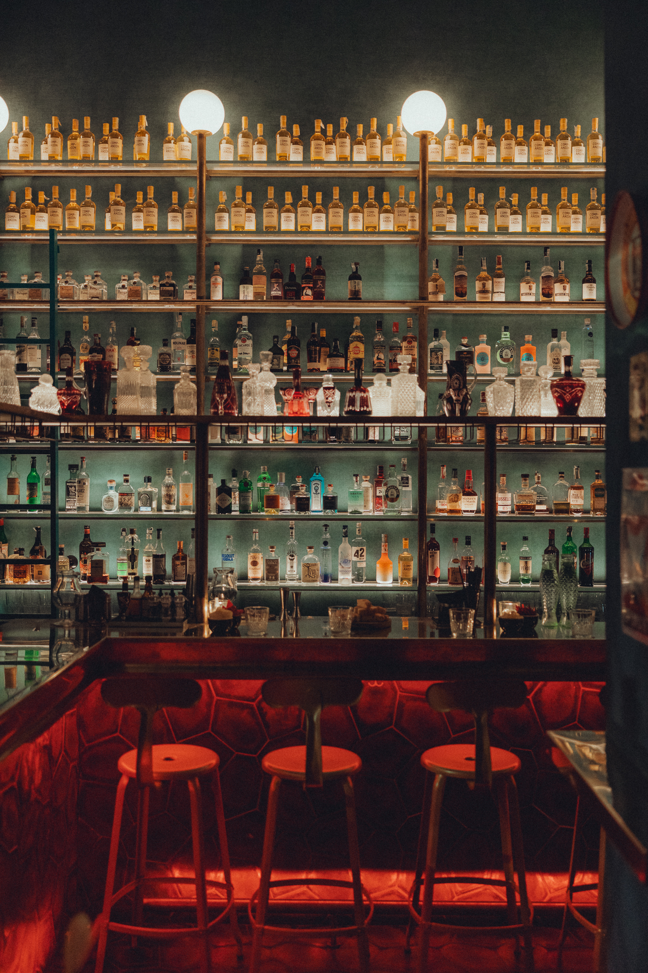 The bar counter with bar stools, on the wall are shelves with a wide selections of different liquors.